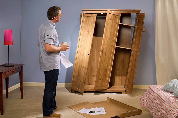 Homme inspectant une armoire en bois, partiellement montée, dans une chambre.
